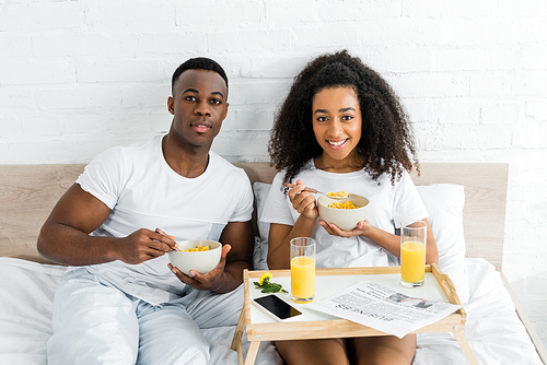 cheerful african american couple eating breakfast in bad and 