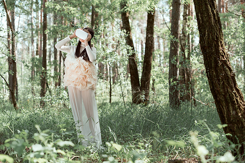 tender woman in white swan costume and vr headset standing on forest background