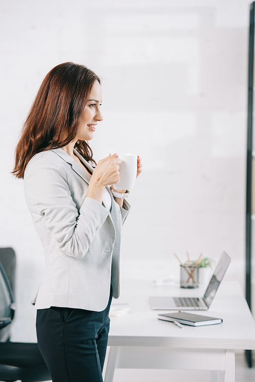 attractive, young secretary looking away while holding coffee cup