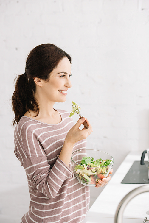 attractive, cheerful woman looking away while eating vegetable salad