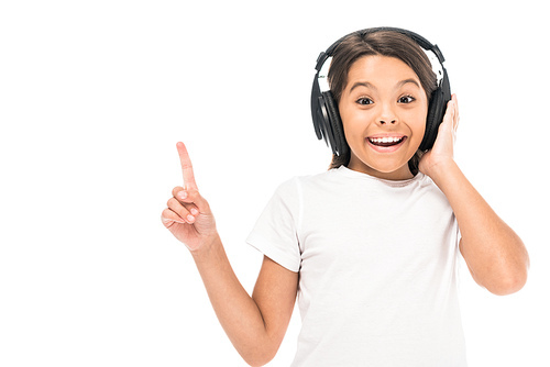 happy kid listening music in headphones and pointing with finger isolated on white