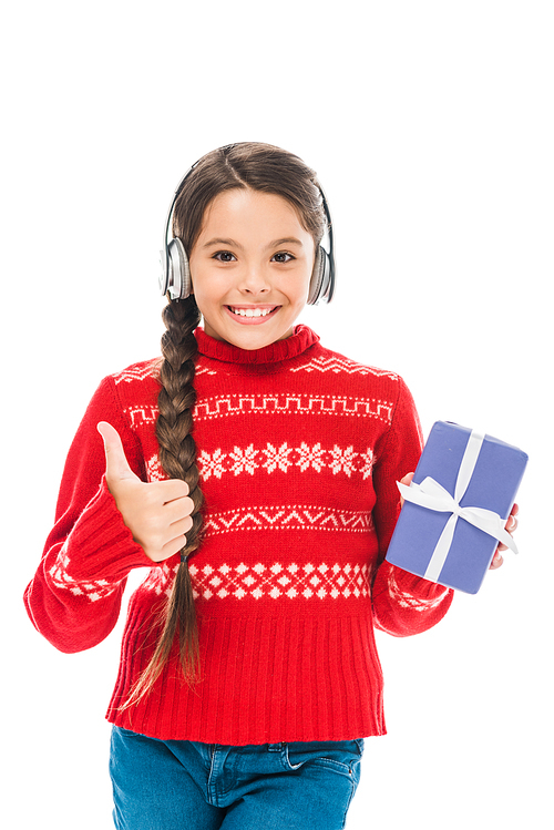 happy kid in sweater holding present and listening music while showing thumb up isolated on white