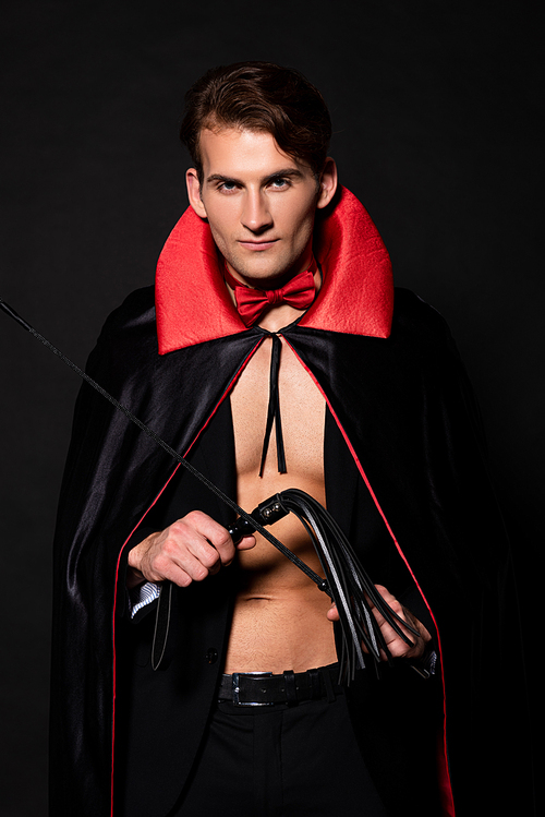 handsome man in vampire halloween costume holding flogging whip isolated on black