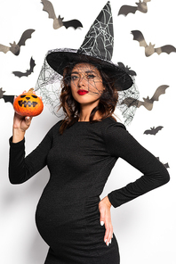 pregnant woman in witch hat holding pumpkin in Halloween