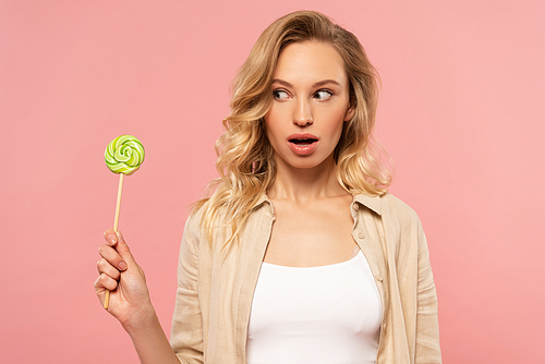 Exited woman looking at lollipop isolated on pink