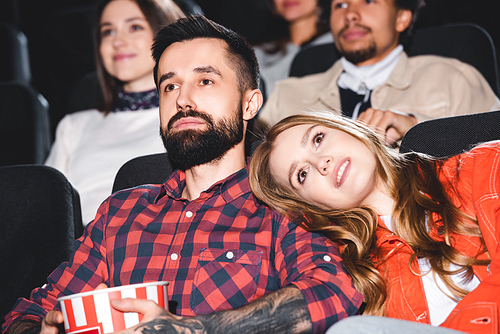 attractive girlfriend lying on shoulder of handsome boyfriend and watching movie in cinema