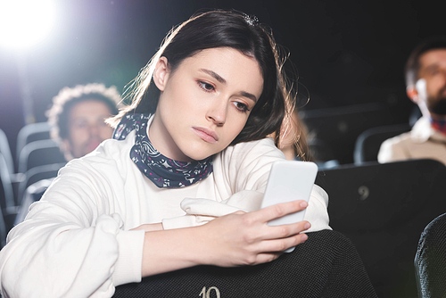 selective focus of sad woman using smartphone in cinema