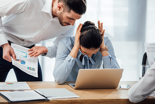 Selective focus of businessman pointing at papers near mexican colleague cowering ears in office