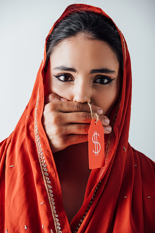 Male hand holding price tag with dollar sign and covering mouth to crying indian woman in sari isolated on grey