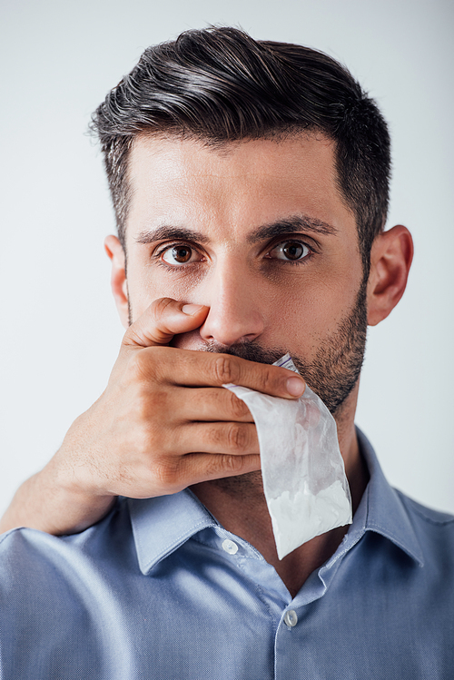 Male hand holding package with cocaine while covering mouth to man isolated on grey