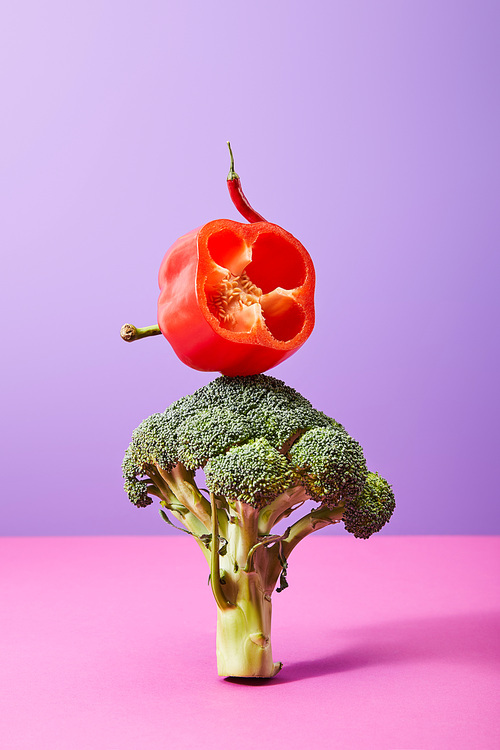 chili pepper and fresh half of bell pepper on broccoli on purple and pink