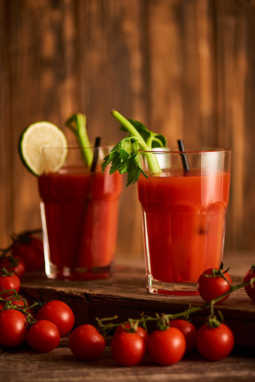 selective focus of bloody mary cocktail in glasses with lime and celery on wooden background with tomatoes