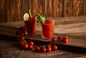 bloody mary cocktail in glasses with lime and celery on wooden background with tomatoes