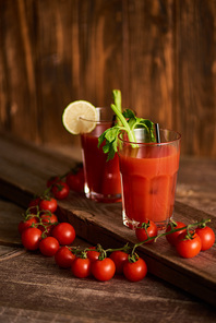 bloody mary cocktail in glasses with lime and celery on wooden background with tomatoes