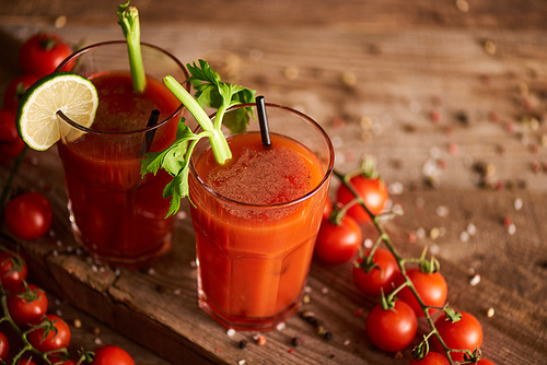 bloody mary cocktail in glasses on wooden background with salt, pepper, tomatoes and celery