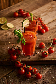 selective focus of bloody mary cocktail in glasses on wooden background with salt, pepper, tomatoes and celery