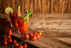 bloody mary cocktail in glasses on wooden background with salt, pepper, tomatoes and celery