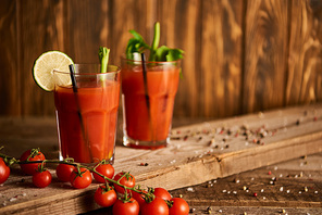 selective focus of bloody mary cocktail in glasses on wooden background with salt, pepper, tomatoes and celery