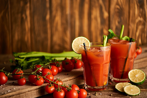 selective focus of bloody mary cocktail in glasses on wooden background with salt, pepper, lime, tomatoes and celery
