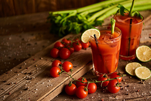 bloody mary cocktail in glasses on wooden background with salt, pepper, lime, tomatoes and celery