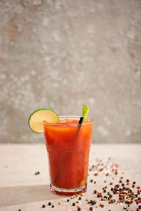 bloody mary cocktail in glass with lime, celery and straw on grey background with black pepper