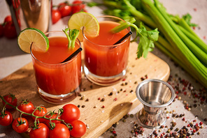 bloody mary cocktail in glasses on wooden board near salt, pepper, lime slices, tomatoes and celery