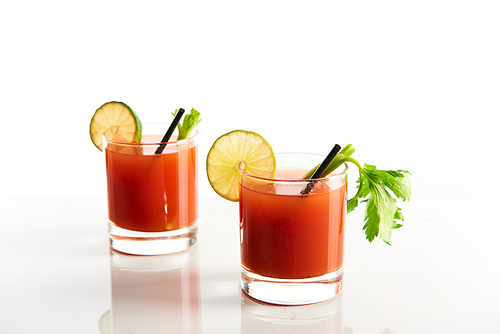 bloody mary cocktail in glasses garnished with lime and celery isolated on white
