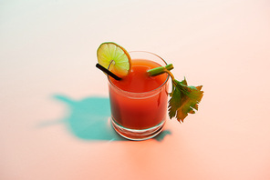 bloody mary cocktail in glass garnished with lime and celery on red and blue illuminated background