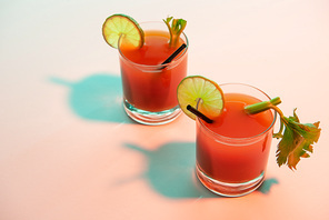 bloody mary cocktail in glasses garnished with lime and celery on red and blue illuminated background