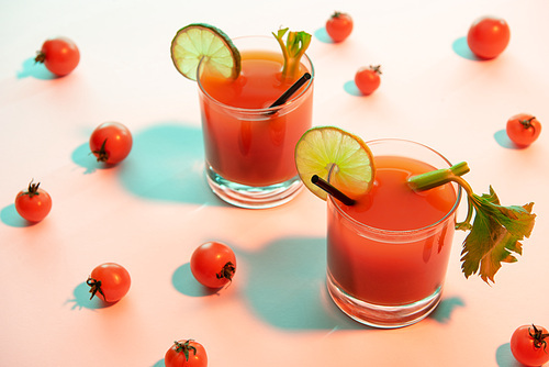 bloody mary cocktail in glasses garnished with lime and celery on illuminated background with tomatoes