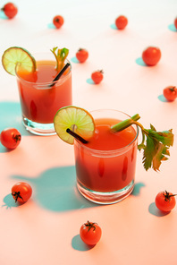 selective focus of bloody mary cocktail in glasses garnished with lime and celery on illuminated background with tomatoes