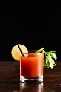 bloody mary cocktail in glass garnished with lime and celery isolated on black