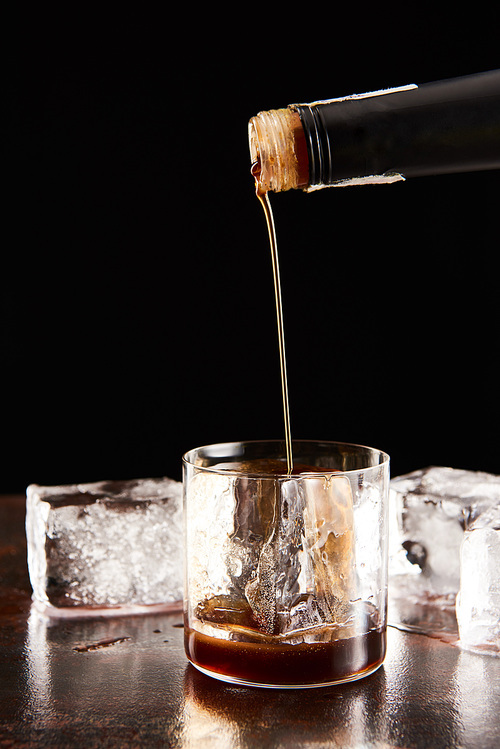 coffee liquor poring in glass with ice cubes isolated on black
