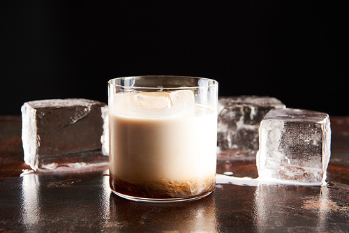 white russian cocktail in glass near ice cubes isolated on black