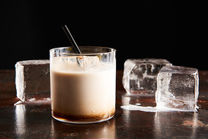 white russian cocktail in glass near melting ice cubes isolated on black