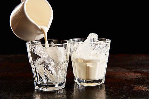 milk pouring in glass with ice cubes isolated on black