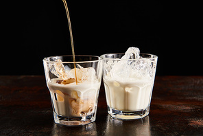 coffee liquor poring in glasses with ice cubes isolated on black
