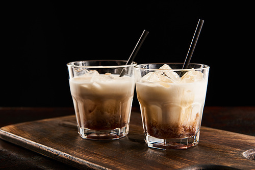white russian cocktail in glasses with straws on wooden board isolated on black
