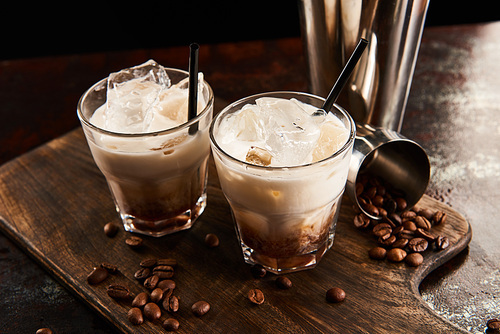 white russian cocktail in glasses with straws on wooden board with coffee grains
