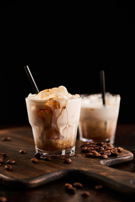 white russian cocktail in glasses with straws on wooden board with coffee grains isolated on black