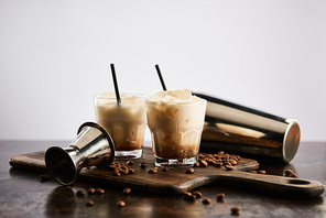 white russian cocktail in glasses with straws on wooden board with coffee grains isolated on grey