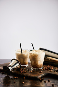white russian cocktail in glasses with straws on wooden board with coffee grains isolated on grey