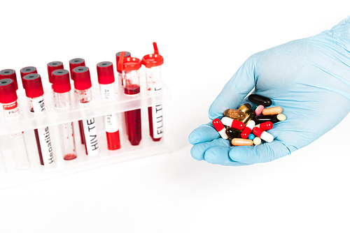 cropped view of scientist in latex glove holding pills near test tubes with lettering isolated on white
