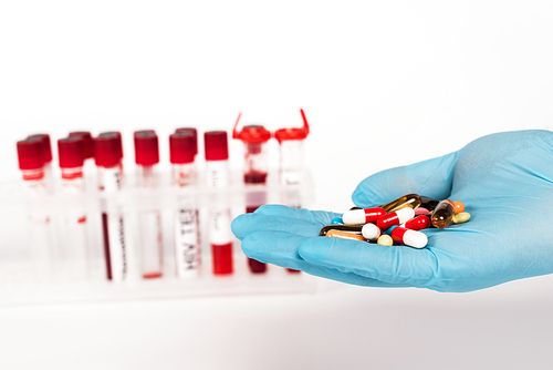 cropped view of scientist in latex glove holding pills near test tubes with lettering on white