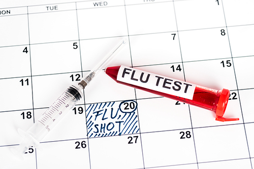 sample with flu test near syringe on calendar with marked date and flu shot lettering