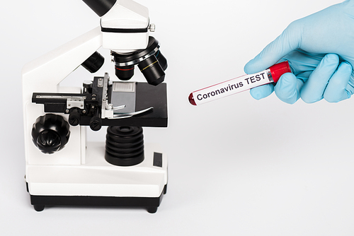 cropped view of scientist holding sample with coronavirus test lettering near microscope isolated on white