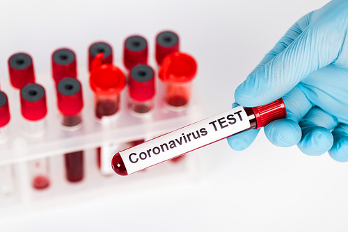 selective focus of scientist holding sample with coronavirus test lettering near test tubes isolated on white