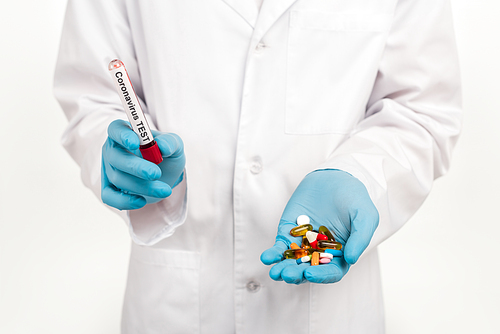 cropped view of scientist holding sample with coronavirus test lettering and pills isolated on white