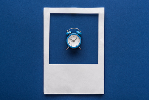 top view of alarm clock in white photo frame on blue background
