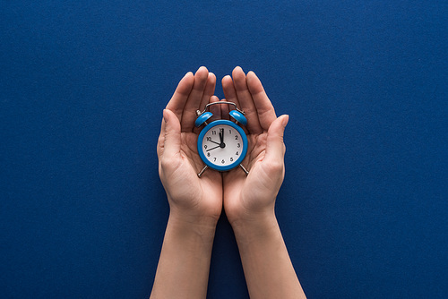 cropped view of woman holding alarm clock on blue background